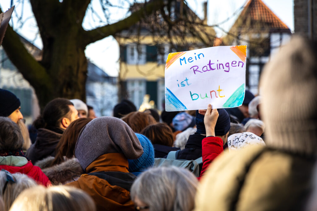 Menschenmenge bei einer Kundgebung, eine Person hält ein Schild mit der Aufschrift ‚Mein Ratingen ist bunt‘ hoch.